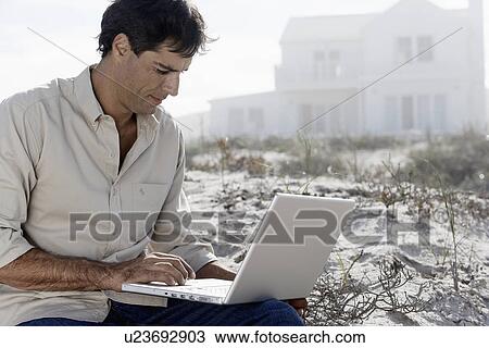 Stock Image - Mature man using laptop at beach. Fotosearch