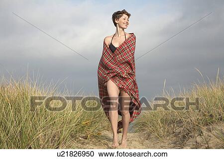 Stock Image - Woman wrapped in blanket walking on path. Fotosearch