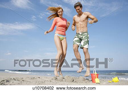 Stock Image - Young couple jumping on sandcastle. Fotosearch