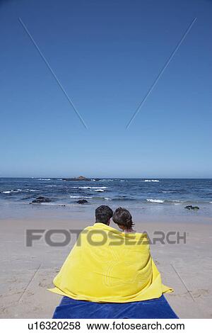 Stock Photo - Young couple wrapped in a towel on beach. Fotosearch
