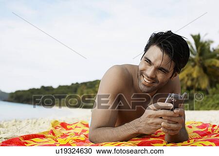 Stock Image - Young man using mobile phone on beach, St. John, US Virgin Islands, USA. Fotosearch