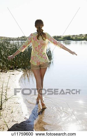Stock Image - Young woman walking in lake with arms outstretched. Fotosearch