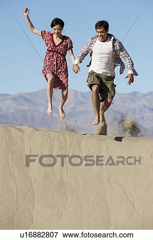 Couple jumping on sand, mountains in background View Large Photo Image Stock Photo - Couple jumping on sand, mountains in background. Fotosearch