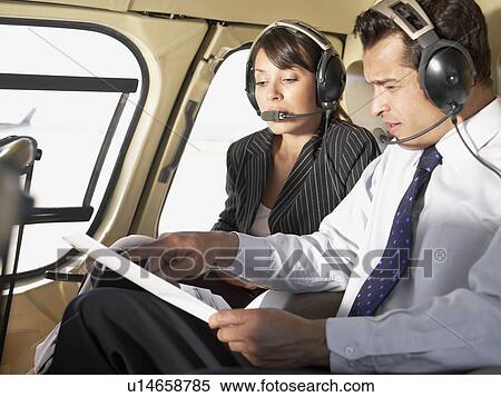 Stock Photography - Two businesspeople wearing headsets and talking in helicopter. Fotosearch