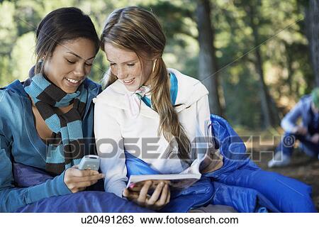 Stock Image - Two teenage girls reading text message in forest. Fotosearch