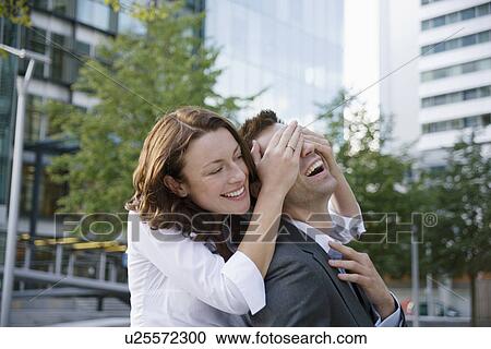 Stock Image - Woman surprising man from behind. Fotosearch