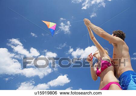 Stock Photograph - Young couple flying kite (low angle view). Fotosearch