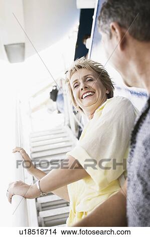 Picture - Low angle view of a mature woman standing on the staircase of a cruise ship and smiling. Fotosearch