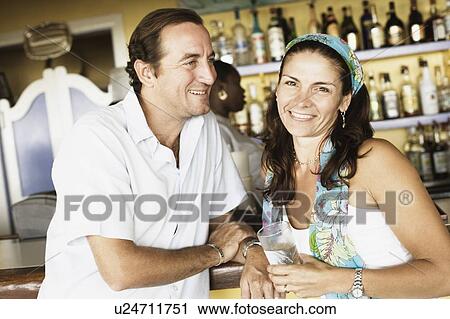 Stock Image - Mid adult couple at a bar counter and smiling. Fotosearch