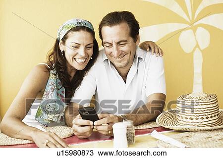 Stock Image - Mid adult couple reading text message on a mobile phone in a restaurant. Fotosearch