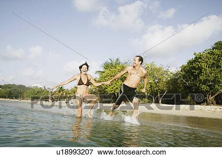 Mid adult couple running in water on the beach View Large Photo Image Stock Photo - Mid adult couple running in water on the beach. Fotosearch