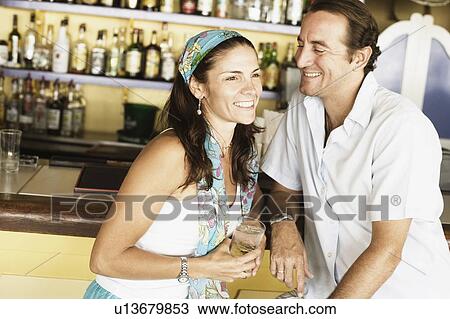 Mid adult couple sitting at a bar counter and smiling View Large Photo Image Stock Image - Mid adult couple sitting at a bar counter and smiling. Fotosearch
