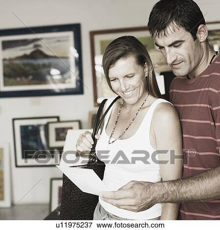 Stock Photo - Mid adult couple standing in a paintings store and smiling. Fotosearch