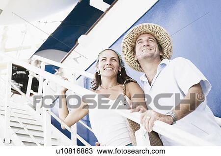 Stock Image - Mid adult couple standing on the staircase of a cruise ship and smiling. Fotosearch