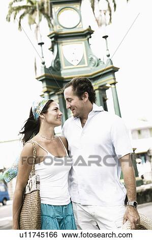 Stock Photograph - Mid adult couple standing with their arms around each other and smiling. Fotosearch