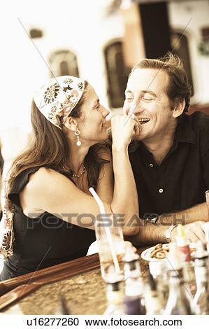 Stock Image - Mid adult woman feeding food to a mid adult man and smiling. Fotosearch