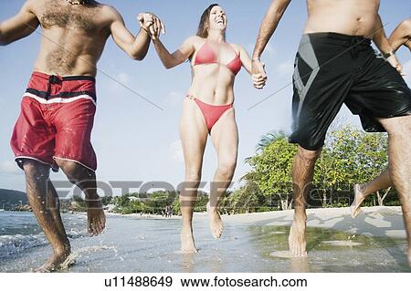 Stock Photo - Mid adult woman running with her friends on the beach. Fotosearch
