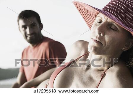 Stock Photo - Mid adult woman with her eyes closed and a mid adult man sitting beside her. Fotosearch
