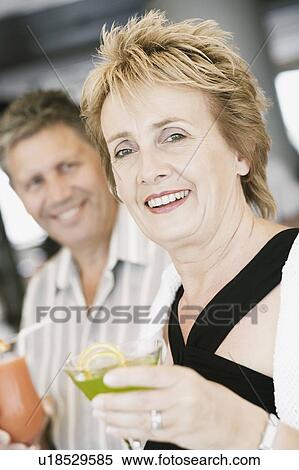 Stock Photography - Portrait of a mature woman holding a glass of cocktail with a senior man beside her. Fotosearch