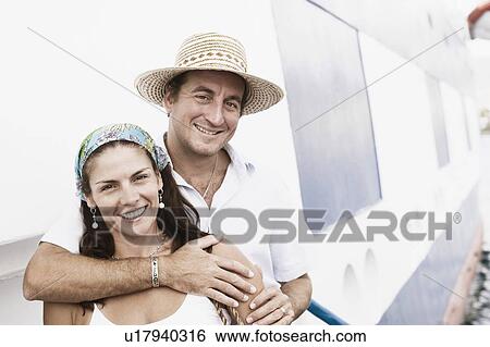 Stock Photograph - Portrait of a mid adult man embracing a mid adult woman from behind and smiling. Fotosearch