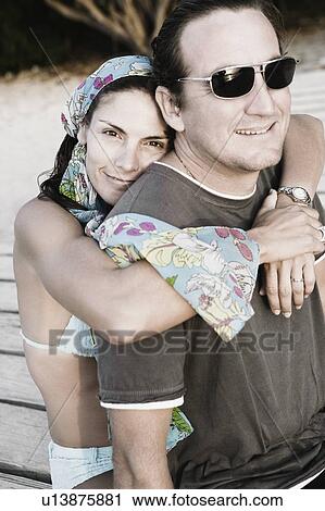 Stock Image - Portrait of a mid adult woman embracing a mid adult man from behind and smiling. Fotosearch