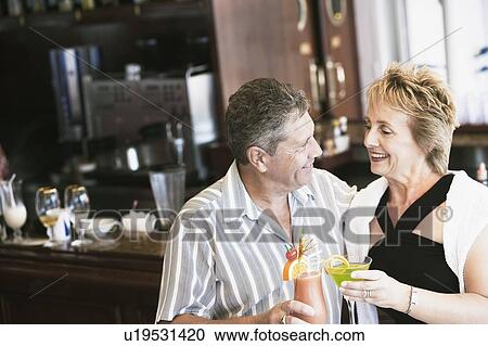 Senior man and a mature woman holding glasses of cocktail and standing at a bar counter View Large Photo Image Stock Image - Senior man and a mature woman holding glasses of cocktail and standing at a bar counter. Fotosearch