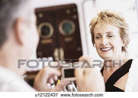 Stock Photo - Senior man taking a picture of a mature woman with a digital camera and smiling. Fotosearch