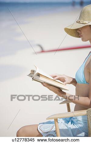 Stock Photography - A young woman reading book at beach. Fotosearch