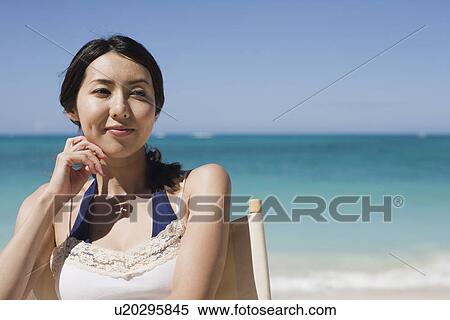 Stock Photography - A young woman sitting on chair at beach. Fotosearch