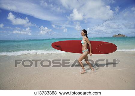 A young woman walking on beach with surfboard View Large Photo Image Stock Photo - A young woman walking on beach with surfboard. Fotosearch