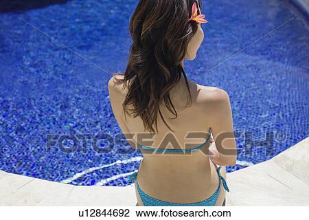 Stock Image - Elevated view of a woman sitting beside swimming pool. Fotosearch