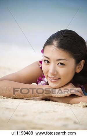 Portrait of a young woman lying on sand at beach View Large Photo Image Stock Photo - Portrait of a young woman lying on sand at beach. Fotosearch