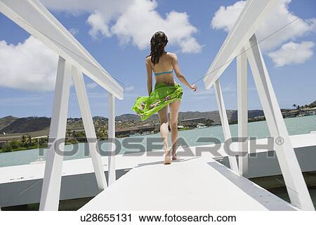 Stock Image - Rear view of a woman walking on a pier. Fotosearch