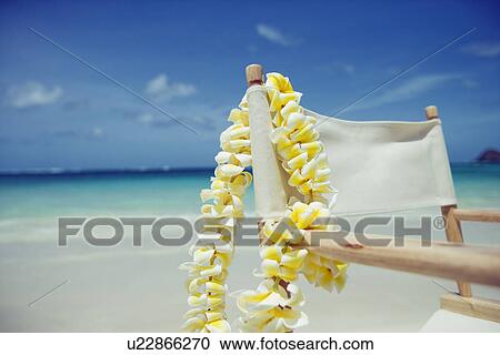 Stock Image - View of a flower garland hanging on wooden chair at beach. Fotosearch