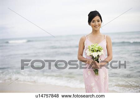 Stock Photo - View of a young woman holding flowers at beach. Fotosearch