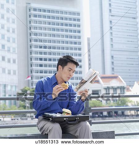 Businessman eating a burger and reading a magazine View Large Photo Image Stock Image - Businessman eating a burger and reading a magazine. Fotosearch