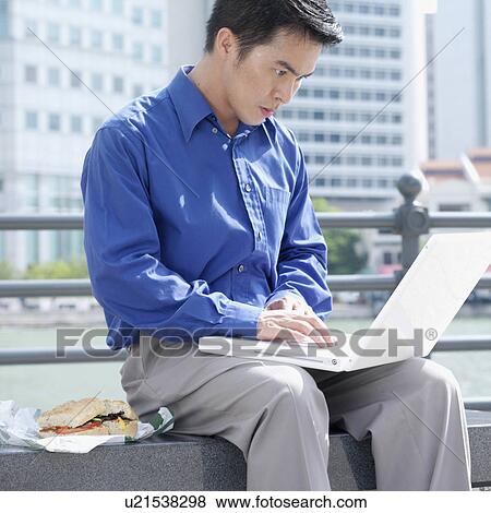 Stock Photo - Businessman sitting on a bench using a laptop. Fotosearch