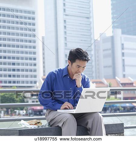 Businessman sitting on a bench using a laptop View Large Photo Image Stock Photography - Businessman sitting on a bench using a laptop. Fotosearch