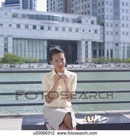 Stock Image - Businesswoman holding a sandwich in front of a railing. Fotosearch