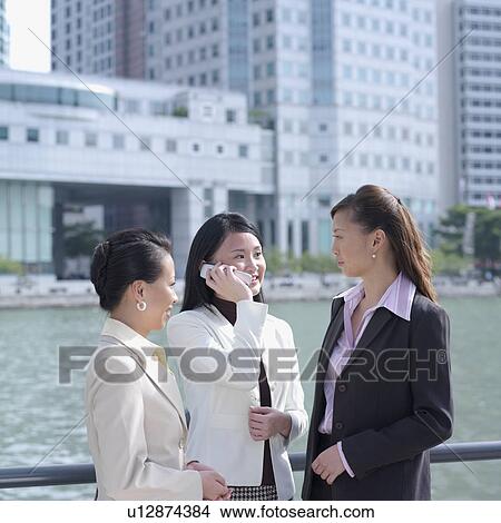 Businesswoman talking on a mobile phone standing beside two businesswomen View Large Photo Image Picture - Businesswoman talking on a mobile phone standing beside two businesswomen. Fotosearch