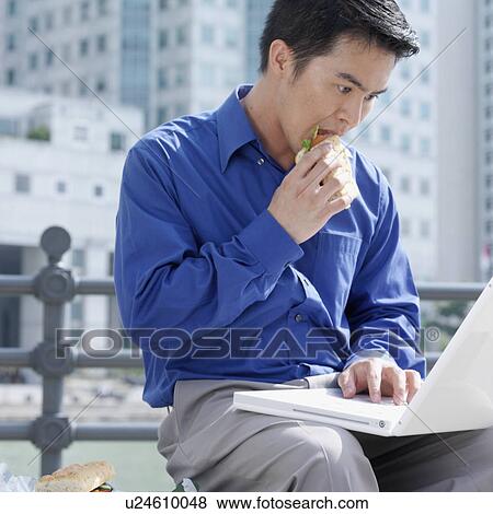 Close-up of a businessman eating a burger using a laptop View Large Photo Image Stock Photo - Close-up of a businessman eating a burger using a laptop. Fotosearch