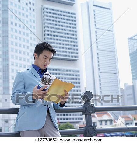 Stock Image - Low angle view of a businessman reading a magazine. Fotosearch