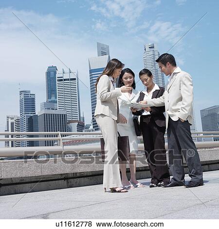 Stock Photo - Low angle view of a businessman showing document to three businesswomen. Fotosearch