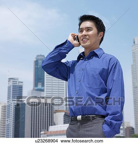 Picture - Low angle view of a businessman talking on a mobile phone. Fotosearch