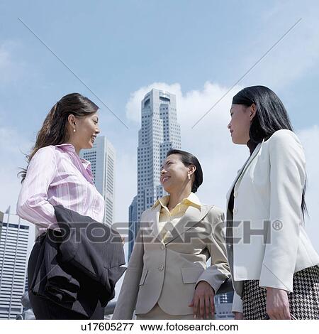Stock Photo - Low angle view of three businesswomen talking to each other. Fotosearch