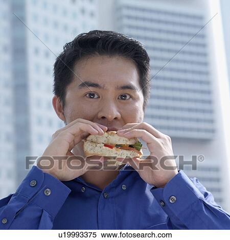 Stock Photography - Portrait of a businessman eating a burger. Fotosearch
