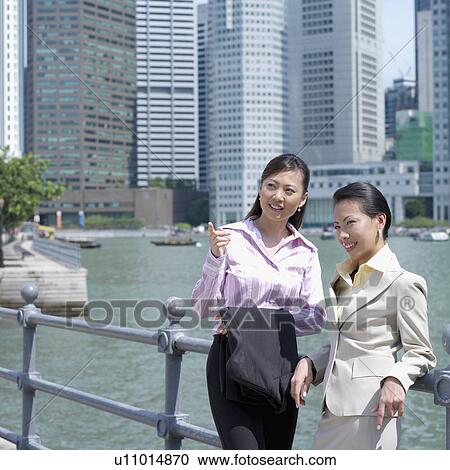 Stock Image - Two businesswomen leaning against a railing. Fotosearch