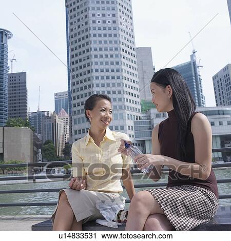 Two businesswomen sitting on a bench talking View Large Photo Image Stock Image - Two businesswomen sitting on a bench talking. Fotosearch