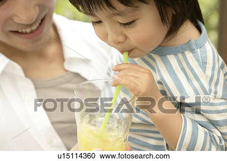 Stock Image - A young boy makes bubbles out of the juice as his father holds him. Fotosearch