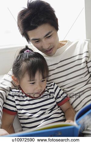 Stock Image - A young farther reading a book to his daughter. Fotosearch